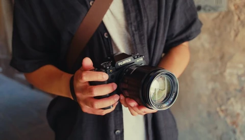Photographer holding a black Fujifilm camera with a telephoto lens against their chest.