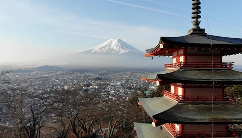 Red pagoda with snow-capped mountain peak in the distance beyond a sprawling city landscape.