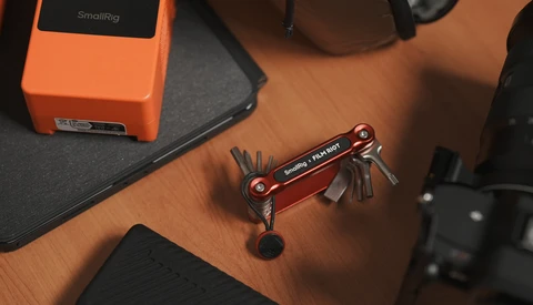 Red multi-tool with extended tools displayed on wooden surface surrounded by photography equipment.