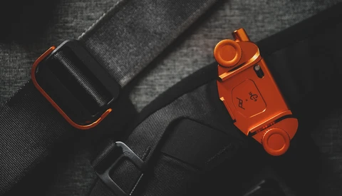 Orange and black camera equipment arranged on gray fabric with dramatic side lighting.