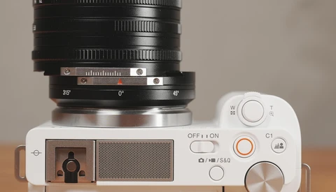 Top-down view of a white mirrorless camera with a large black telephoto lens mounted, showing controls and aperture ring.