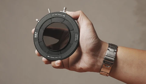Person holding a telephoto lens with focus distance markings and depth-of-field scale visible on the barrel.