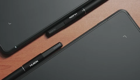 Two black stylus pens labeled with text, arranged diagonally on a wooden surface next to tablet devices.