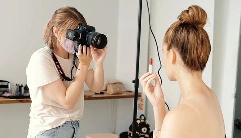 Photographer with camera on tripod shooting a portrait of a shirtless male model in a studio setting.