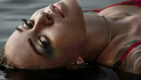 Male portrait with head tilted back, eyes closed, wearing chain necklace in shallow water.