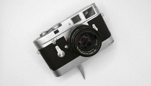 Vintage rangefinder camera with chrome top plate and black body on white background.