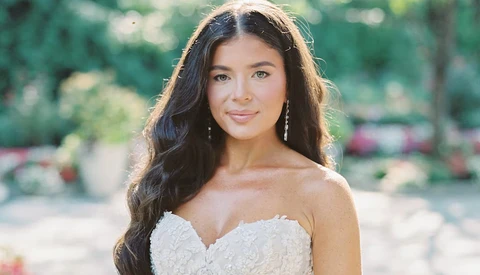 Woman in beaded white strapless gown with long dark wavy hair, photographed outdoors in natural sunlight.