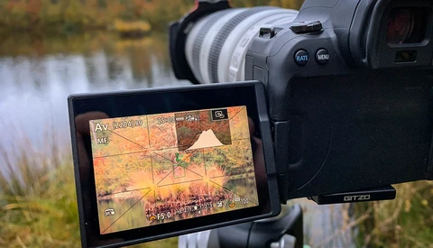 External monitor displaying video footage with grid overlay and exposure information mounted on professional video camera beside water landscape.