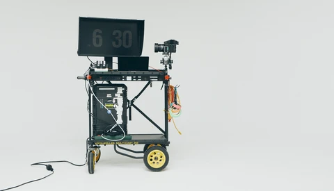 Mobile teleprompter rig on yellow-wheeled cart with monitor displaying timecode display.