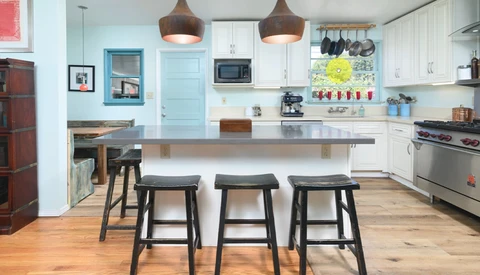 Modern kitchen with white cabinetry, dark wood island with three black stools, and pendant lights overhead.