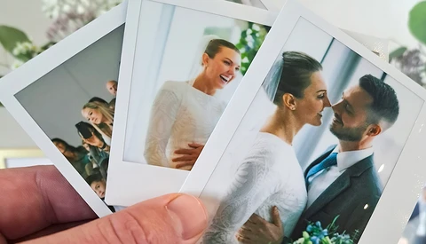 Hand holding instant film photographs of people in various candid moments and poses.