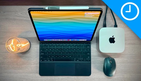 Flat lay of a tablet with colorful wallpaper, wireless mouse, Mac mini, and desk lamp on wood surface.