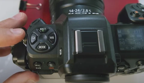 Close-up of camera control dial showing BKT, WB, and MODE buttons with lens labeled 14-24/2.8 S in background.