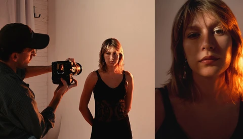 Filmmaker operating a vintage camera while photographing a woman in a black tank top against a white wall.