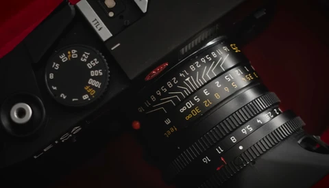 Overhead view of a rangefinder film camera with manual focus lens on dark surface with red fabric.