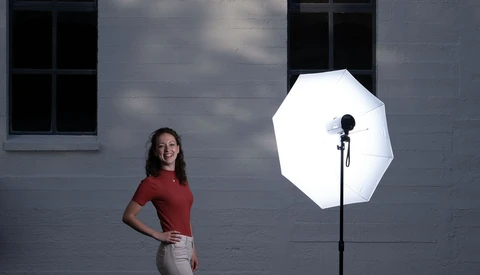 Woman in red shirt posing against gray brick wall lit by large octagonal softbox.