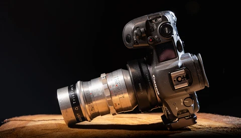Vintage film camera with telephoto lens mounted on wooden surface against black background.