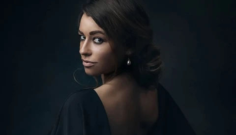 Woman with dark hair looking over shoulder against dark background.