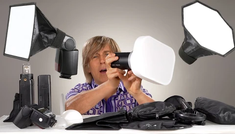 Photographer examines camera flash and softbox diffuser among studio lighting equipment.
