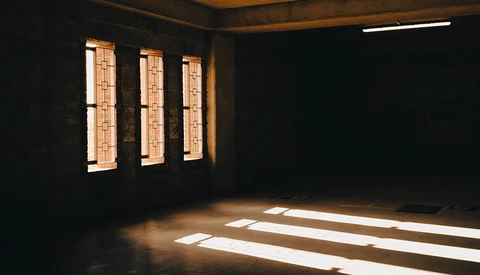 Sunlight streaming through three narrow windows into a dark interior space, creating geometric shadows on the floor.