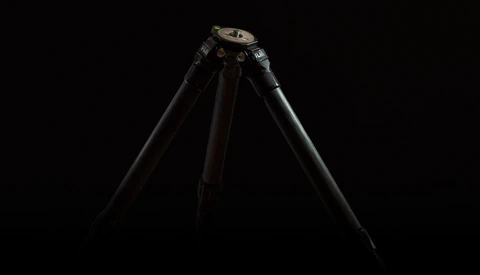 Professional tripod with black legs and metal head against dark background.