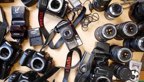 Collection of Pentax film cameras, lenses, flashes, and accessories arranged on a wooden surface.