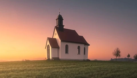 White wooden church with dark roof standing alone in a vast prairie at sunset.