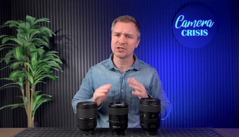 Man in denim shirt demonstrating three camera lenses on a table in a studio setting.