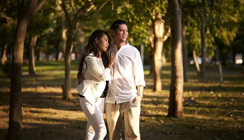 Couple walking together through a tree-lined park during golden hour.