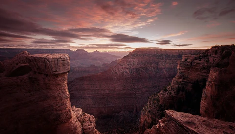 Grand Canyon vista at sunset with layered red rock formations and dramatic pink-orange sky.