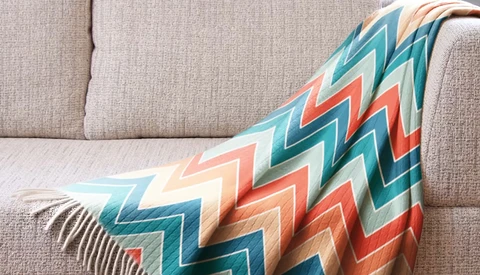 Colorful geometric patterned throw blanket draped over a beige linen sofa.