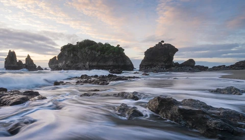 Rocky islands rising from turbulent ocean waves at dusk, with smooth water motion blur in foreground.