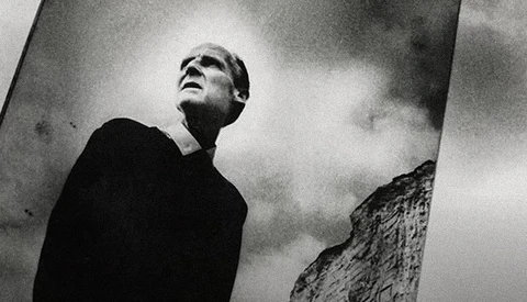 Man in dark clothing gazing upward against dramatic cloudy sky in high-contrast black and white photography.