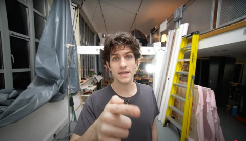 Person pointing at camera inside a narrow RV or camper van with storage shelves and equipment visible.