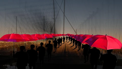 Silhouetted crowd holding bright red umbrellas on a wet bridge at dusk.