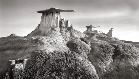 Dramatic black and white landscape of distinctive rock formations with flat-topped peaks rising from eroded badlands terrain.