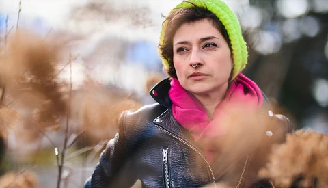 Woman in neon yellow beanie and magenta jacket looking away in autumn setting.