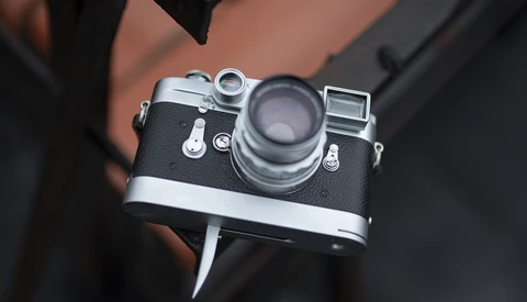Vintage rangefinder camera with chrome and black body held in hands against dark clothing.