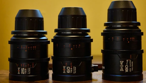 Three black cinema prime lenses with red markings arranged side-by-side against a yellow background.