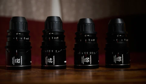 Four black cinema lenses arranged in a row on a wooden surface against a burgundy backdrop.