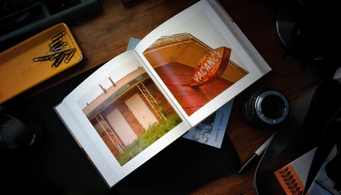 Open portfolio displaying architectural photography prints on a wooden desk with camera equipment nearby.