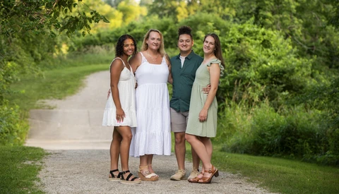Four people standing together on a tree-lined dirt path in natural daylight.
