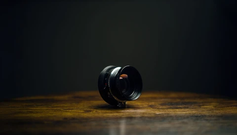 Black camera lens with orange reflections positioned on a wooden surface against a dark background.
