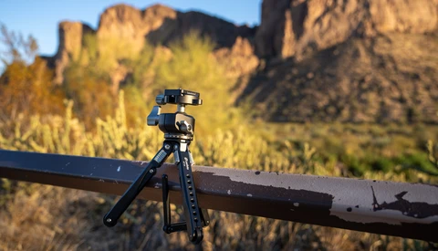 Compact tripod with smartphone mount positioned on a metal rail overlooking desert mountains.