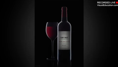 Wine bottle and filled glass against a black background with dramatic side lighting.