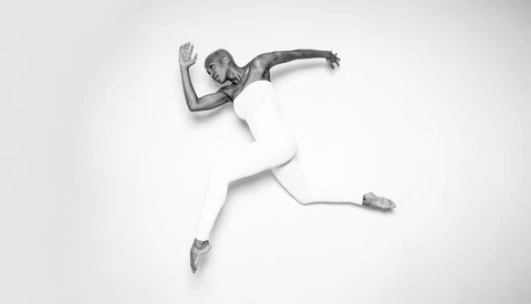 Overhead view of a person in white clothing performing a dynamic jumping pose against a white background.
