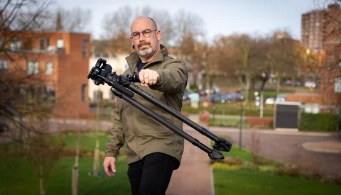 Man holding a camera stabilizer rig with mounted camera and lens in an urban park setting.