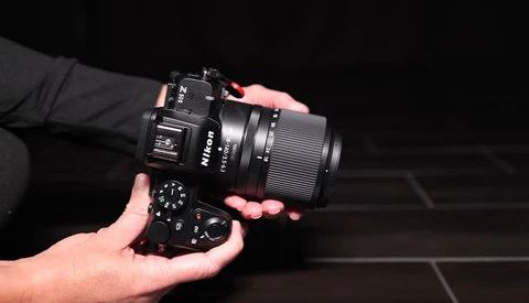 Photographer's hands holding a black mirrorless camera with attached lens against a dark background.
