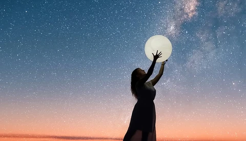 Silhouetted figure reaching toward a glowing full moon against a starry night sky with the Milky Way visible.