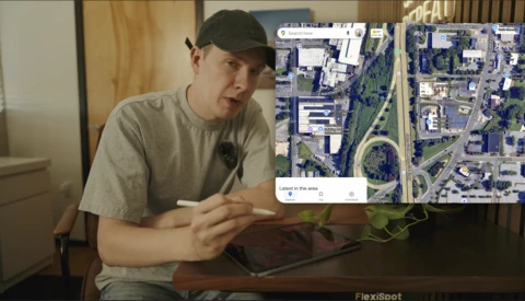 Person gesturing toward aerial satellite map displayed on tablet screen.